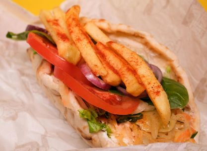 Delicious gyros with fried potatoes and sliced tomatoes with red onion and green leaves with cabbage leaves in pita on paper on yellow background